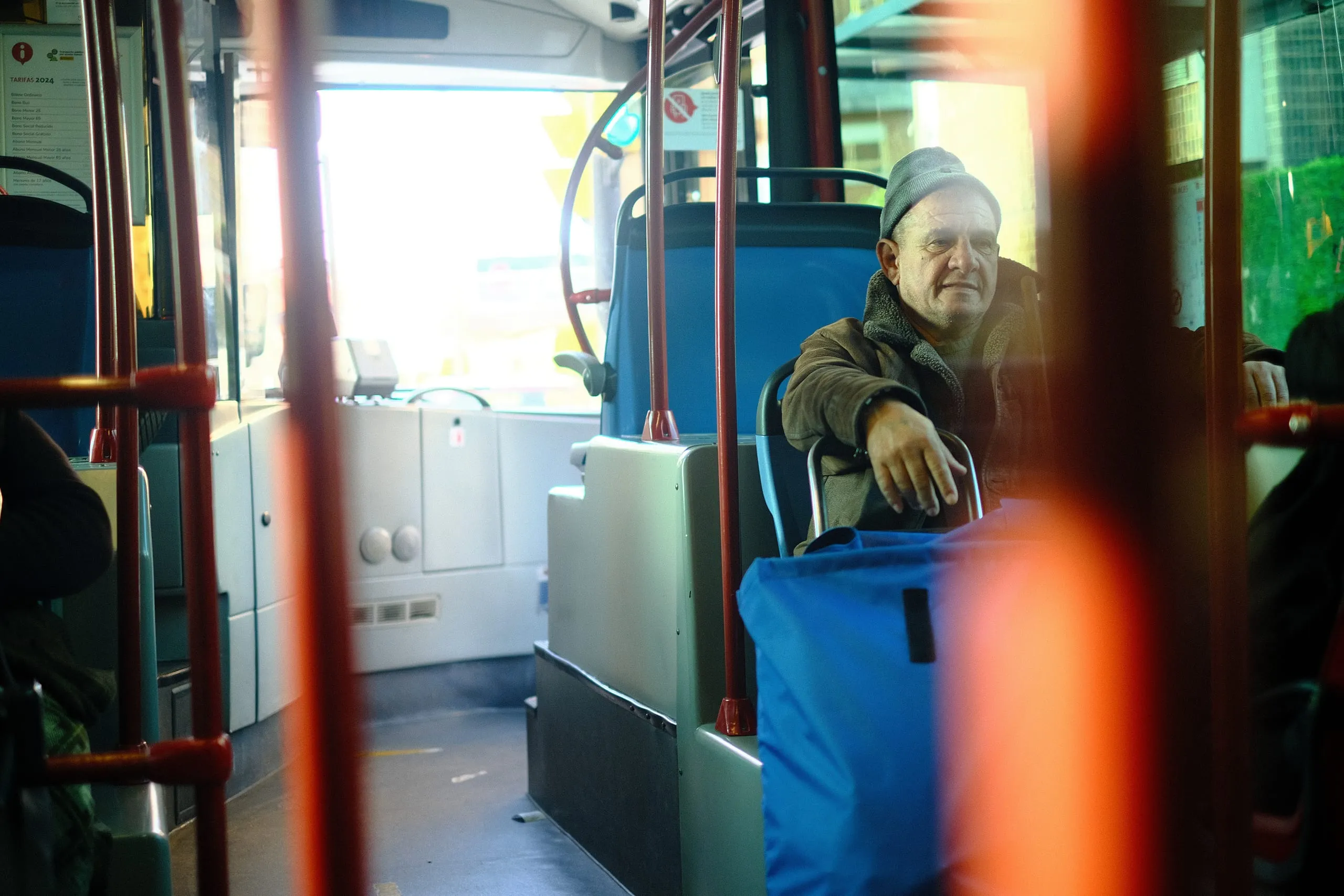 A man sits with his luggage aboard a bus in winter sun