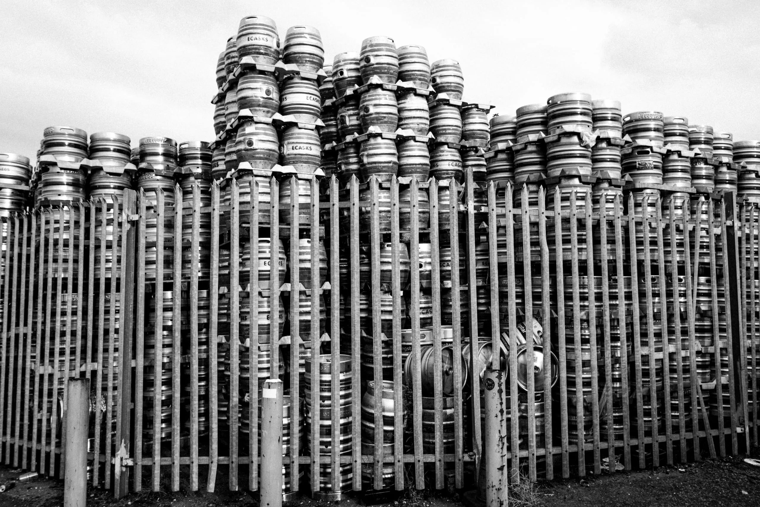 Stacked metal beer kegs piled behind a palisade fence