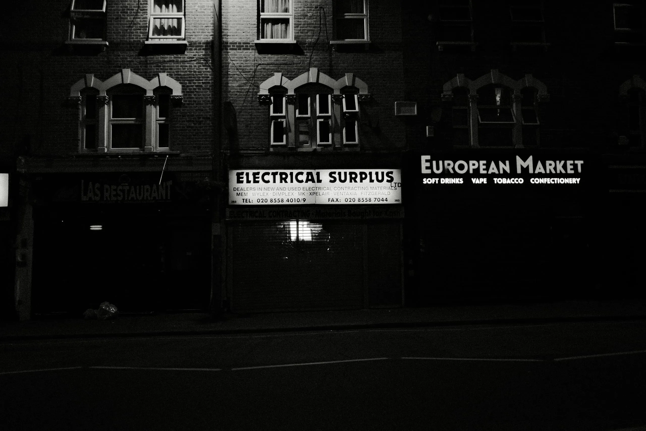 Shuttered shopfronts including European Market and Electrical Surplus at night, Leyton High Road