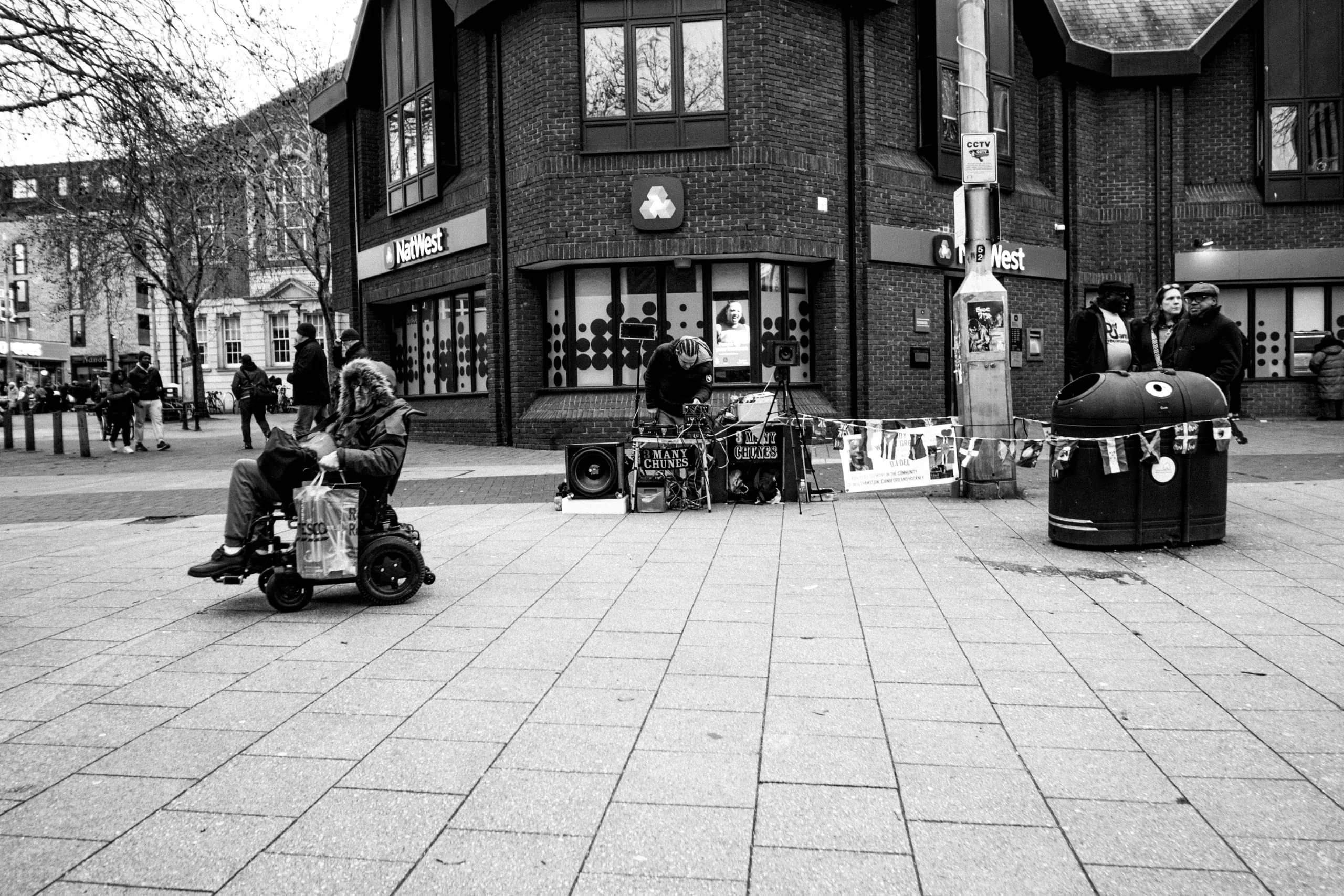 A street musician performs by a NatWest bank as a man on a mobility scooter passes by
